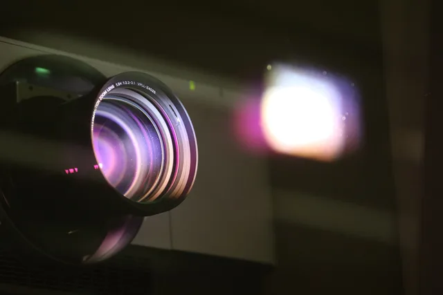 Close-up view of a projector lens with light reflections, highlighting optics and technology. Teleprompter app or beam-splitter rig? Eye-line, setup and scripts